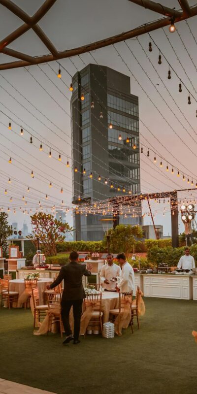 Elegant rooftop event with tables and lights set against Mumbai skyline at sunset, India.
